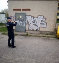 zdjęcie kolorowe na którymi policjanta kontrolującego rejon i fotografującego graffiti