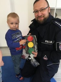 zdjęcie kolorowe na którym widać policjanta z chłopczykiem  ze żłobka