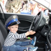 zdjęcie na którym chłopiec siedzi w radiowozie trzyma za kierownicę i ma czapkę policjanta