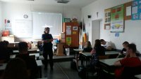 zdjęcie na którym widać jak policjant przeprowadza prelekcje w klasie z uczniami i wyświetlona jest w tle prezentacja multimedialna