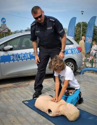 dziecko pod okiem policjanta przeprowadza  masaż klatki piersiowej na fantomie