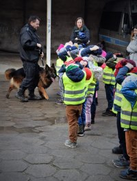 dzieci zwiedzają teren komendy policji na zdjęciu również policjant z psem służbowym