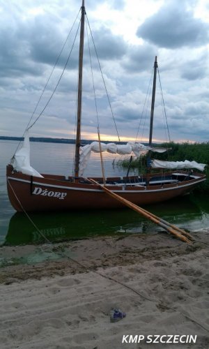 Przycumowana do brzegu łódź masztowa, w tle akwen i fragment plaży