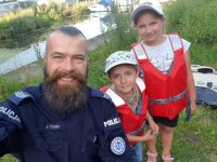 Policjant na wspólnym zdjęciu z dziećmi ubranymi w czerwone kamizelki ratunkowe