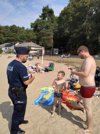 Policjant rozdający materiały profilaktyczne wypoczywającym na szczecińskich kąpieliskach