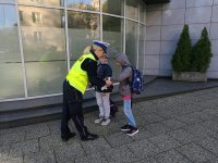 POLICJANTKA ROZDAJE ULOTKI I ODBLASKI DZIECIOM